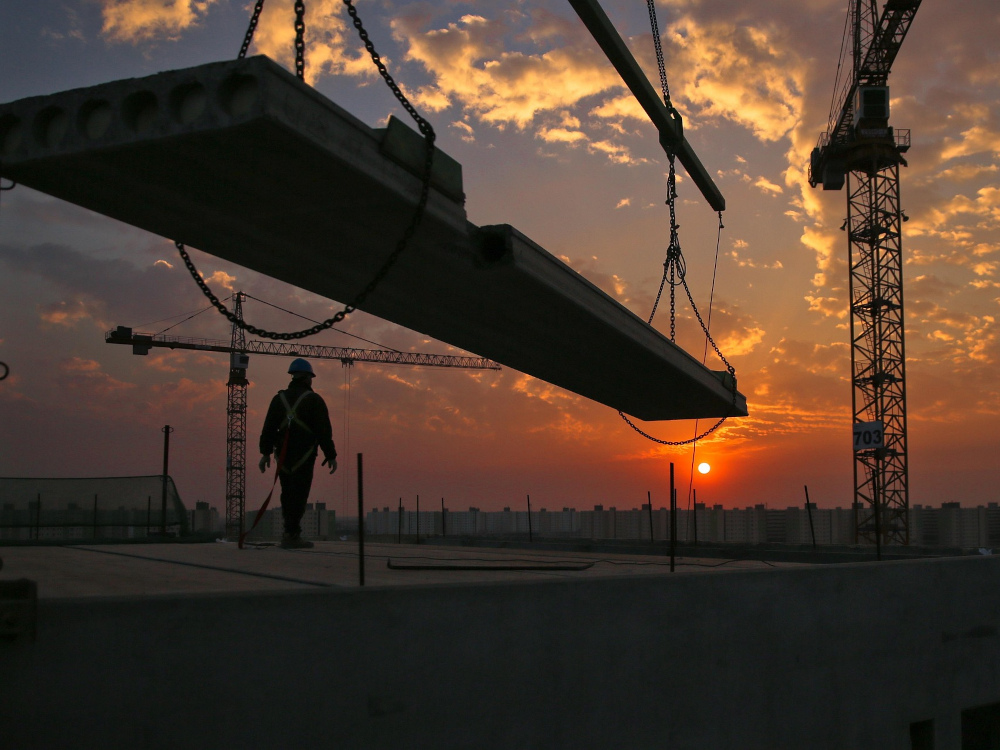 empreiteiro em cima de um edifício em construção com grua por cima no por do sol