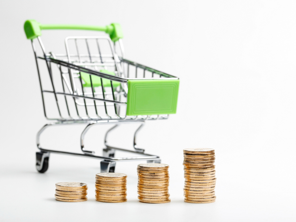 carrinho de compras em fundo branco com montinhos de moedas na frente